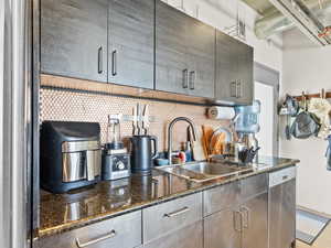 Kitchen featuring stainless steel dishwasher, decorative backsplash, and dark stone countertops