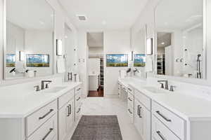 Bathroom with a walk in closet, two vanities, marble finish floors, a shower stall, and recessed lighting