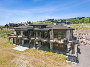 Rear view of property featuring stone siding, a patio area, stairway, and a standing seam roof