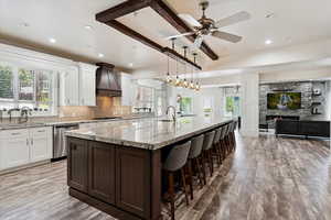 Kitchen with appliances with stainless steel finishes, custom range hood, a spacious island, light wood-style floors, and recessed lighting