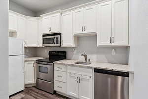 Kitchen with appliances with stainless steel finishes, dark wood-style flooring, and white cabinetry