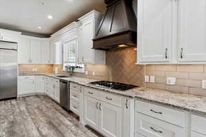 Kitchen with appliances with stainless steel finishes, premium range hood, white cabinets, and recessed lighting