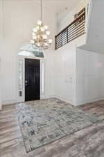 Foyer entrance featuring a decorative wall, a chandelier, wood finished floors, a high ceiling, and crown molding