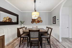 Dining room featuring light wood-style floors, arched walkways, crown molding, wainscoting, and a decorative wall