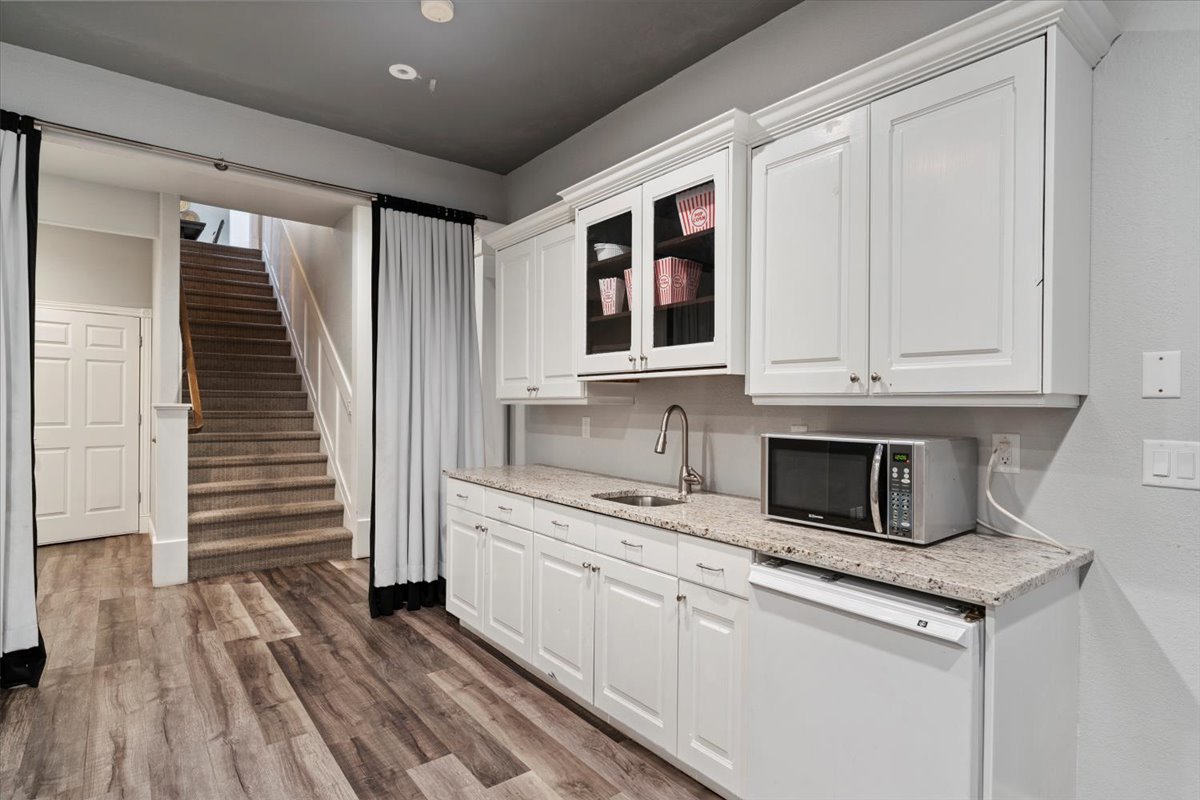 Kitchen with white dishwasher, white cabinets, wood finished floors, and glass insert cabinets