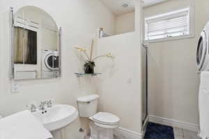 Full bath with tile patterned floors, an enclosed shower, and washer / dryer