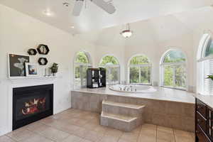 Bathroom with a bath, healthy amount of natural light, a glass covered fireplace, tile patterned floors, and a towering ceiling