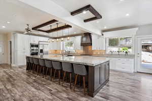 Kitchen with built in appliances, custom exhaust hood, light wood finished floors, decorative backsplash, and beam ceiling