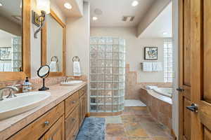 Full bath featuring a bath, double vanity, stone tile floors, a walk in shower, and recessed lighting