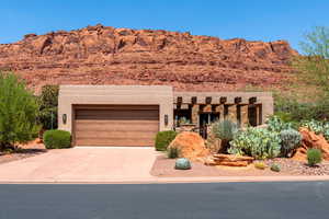 Pueblo-style home featuring an attached garage, driveway, stucco siding, and stone siding
