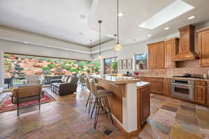 Kitchen featuring stainless steel appliances, stone tile floors, premium range hood, tasteful backsplash, and a skylight