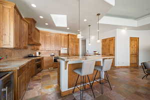 Kitchen featuring stone tile flooring, stainless steel appliances, recessed lighting, decorative backsplash, and a skylight