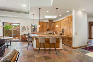 Kitchen with wall chimney exhaust hood, stone tile flooring, decorative backsplash, a breakfast bar area, and recessed lighting
