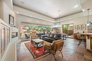 Living room featuring stone tile floors, a tray ceiling, recessed lighting, and a premium fireplace