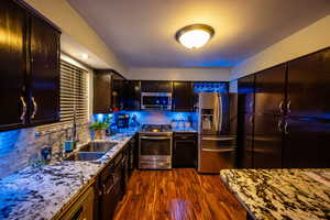 Kitchen featuring appliances with stainless steel finishes, tasteful backsplash, and light stone counters