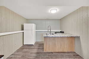 Kitchen featuring freestanding refrigerator, wood walls, light stone countertops, and a peninsula