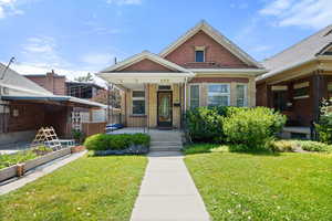 View of front of home with covered porch, a front yard, brick siding, and a garden
