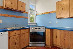 Kitchen with dishwasher, stainless steel gas stove, wood finished floors, tasteful backsplash, and brown cabinetry