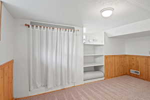 Unfurnished bedroom with wainscoting, wood walls, and a textured ceiling