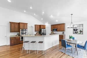 Kitchen with stainless steel appliances, a large island, a chandelier, brown cabinetry, and light wood-style floors
