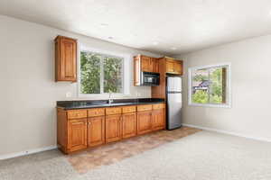 Kitchen featuring freestanding refrigerator, black microwave, brown cabinetry, and dark countertops