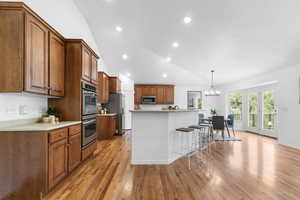 Kitchen with stainless steel appliances, light countertops, brown cabinetry, a breakfast bar area, and recessed lighting