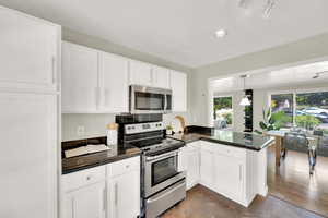 Kitchen with stainless steel appliances, a peninsula, white cabinetry, recessed lighting, and hanging light fixtures