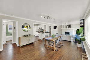 Dining area with dark wood-style flooring, a brick fireplace, and ornamental molding