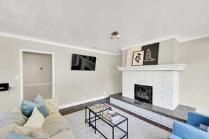 Living room featuring wood finished floors, crown molding, a fireplace, and a textured ceiling