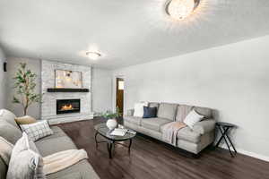 Living area with wood finished floors, a stone fireplace, and a textured ceiling