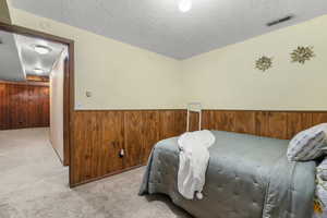 Carpeted bedroom with wood walls, wainscoting, and a textured ceiling