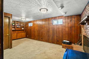 Below grade area featuring wooden walls, a brick fireplace, carpet flooring, a textured ceiling, and built in features