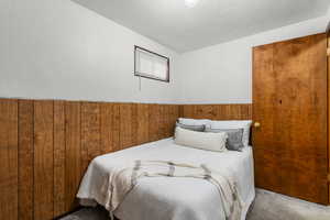 Bedroom with carpet floors, a textured ceiling, and wood walls
