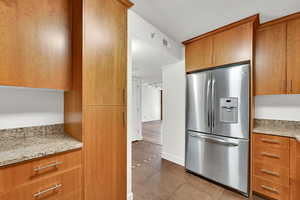 Kitchen featuring stainless steel fridge, tile patterned flooring, brown cabinets, and light stone counters