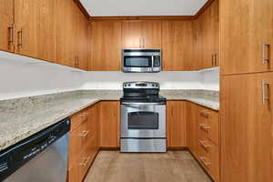 Kitchen featuring appliances with stainless steel finishes, brown cabinets, and light stone counters