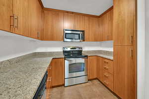 Kitchen with appliances with stainless steel finishes, brown cabinetry, and light stone countertops