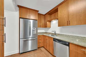 Kitchen with appliances with stainless steel finishes, light stone countertops, light tile patterned floors, and brown cabinetry