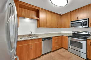 Kitchen with appliances with stainless steel finishes, light stone counters, light tile patterned floors, and brown cabinetry