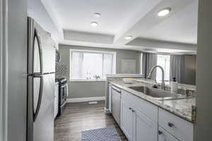 Kitchen featuring a tray ceiling, appliances with stainless steel finishes, dark wood-type flooring, white cabinets, and light stone countertops