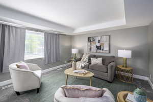 Carpeted living area featuring baseboards and a tray ceiling
