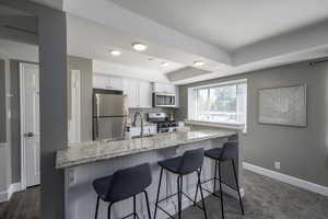 Kitchen with appliances with stainless steel finishes, white cabinets, a breakfast bar, a tray ceiling, and light stone countertops