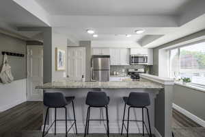 Kitchen with appliances with stainless steel finishes, a breakfast bar, dark wood-style flooring, and white cabinets