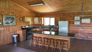 Kitchen featuring freestanding refrigerator, stainless steel gas range, wood ceiling, log walls, and a kitchen breakfast bar