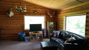 Carpeted living area with vaulted ceiling, wood ceiling, a chandelier, and rustic walls