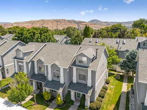 View of front of house featuring stucco siding, a mountain view, a shingled roof, a front lawn, and a residential view