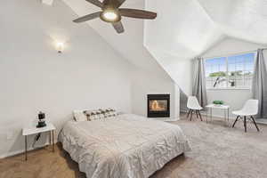 Bedroom with vaulted ceiling, carpet floors, a ceiling fan, a glass covered fireplace, and a textured ceiling