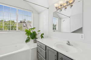 Bathroom featuring a bath, vanity, healthy amount of natural light, vaulted ceiling, and a chandelier