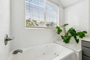 Bathroom with a jetted tub, vaulted ceiling, and vanity