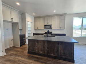 Kitchen with stainless steel microwave, dark countertops, backsplash, dark wood-type flooring, and a kitchen island with sink
