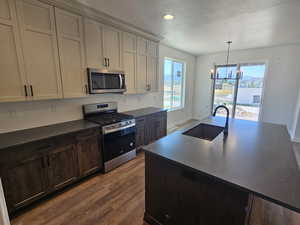 Kitchen featuring appliances with stainless steel finishes, dark countertops, dark wood-style flooring, decorative backsplash, and a chandelier